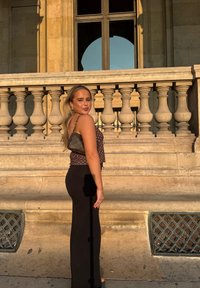 Musta leveälahkeiset housut, jotka on yhdistetty ruskeaan pilkulliseen crop-toppiin. Asua täydentää pieni, muotoiltu käsilaukku ja teksturoitu tausta.