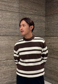Pull rayé brun et blanc avec une texture tricotée, doté d'un col rond et d'une coupe décontractée, porté avec un pantalon foncé.