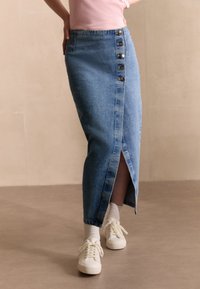 Gonna di jeans di colore azzurro chiaro con spacco frontale, dotata di chiusura a bottone sul lato sinistro e design dritto, alla caviglia.