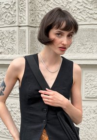 Svart lin sleeveless klänning med knappar fram, med v-ringad halsringning och texturerad kant. Silversmycke av kedja och mörk axelväska.