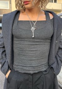 Maiou gri mulat, confecționat din material reiat, purtat sub o haină gri închis, asortat cu pantaloni negri plisati și coliere argintii suprapuse.