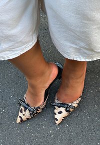 Leopardų rašto smailianos kojų mules su juodu lankeliu ir sidabriniais perlais; blizgus juodas kulnas; lengva medžiaga; kasdieniška vasaros avalynė.