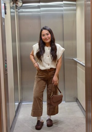 Top de punto crema con textura acanalada y botones; pantalones anchos de pana marrón; bolso marrón; zuecos marrones; fondo de ascensor.