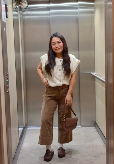 Top de punto crema con textura acanalada y botones; pantalones anchos de pana marrón; bolso marrón; zuecos marrones; fondo de ascensor.