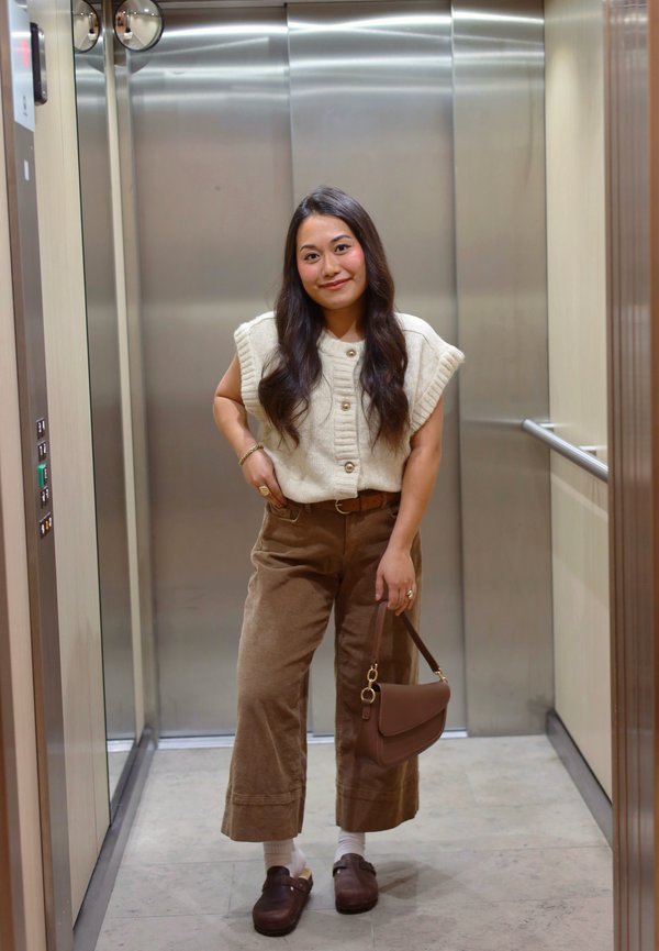 Top de punto crema con textura acanalada y botones; pantalones anchos de pana marrón; bolso marrón; zuecos marrones; fondo de ascensor.