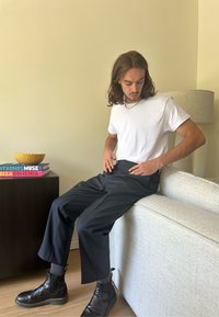 Calças largas pretas feitas de tecido, combinadas com uma t-shirt branca. A modelo usa botas de tornozelo pretas com meias cinzentas. Livros e uma tigela nas proximidades.