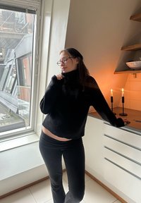 Fekete, kötött garbó és fekete, testhezálló nadrág. Belső tér ablakokkal, modern szekrényekkel és gyertyákkal a pulton.