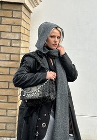 Casaco comprido de couro preto, sweatshirt cinzento com capuz, cachecol cinzento e uma mala de mão preta acolchoada com alça de corrente e detalhes em metal.