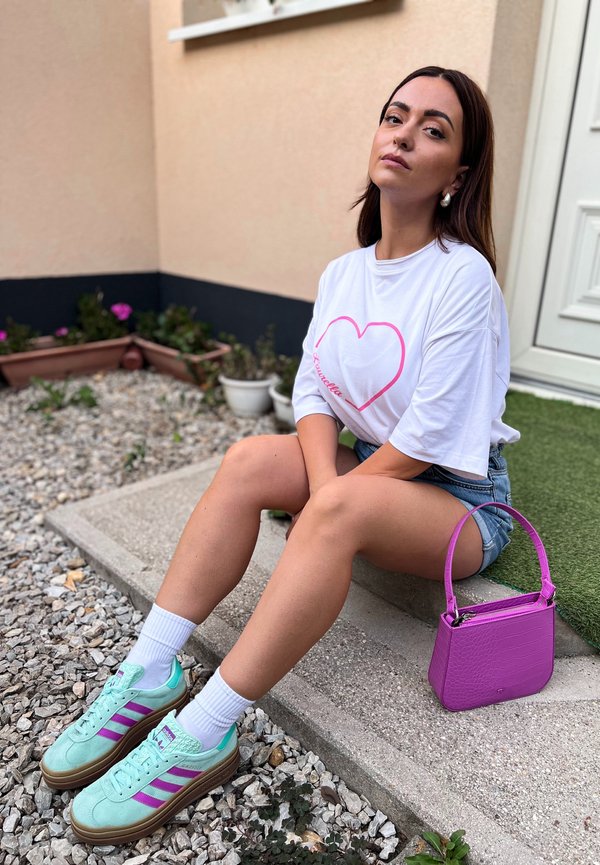 Zapatillas de ante verde claro con rayas rosas, calcetines blancos, pantalones cortos de mezclilla y una camiseta blanca oversized con un diseño de corazón rosa. Bolso morado.