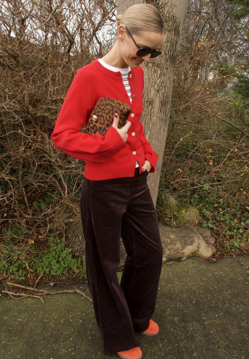 Rød cardigan med gullknapper, stripete topp, brune kordfløyelsvidebukser og oransje sko. Holder en leopardmønstret clutch.