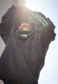 Tumši pelēka vilnas jaka ar strukturētu virsmu. Aprīkota ar zaļiem akcentiem, kabatu ar rāvējslēdzēju un zīmola uzrakstu uz piedurknes.