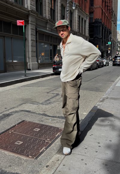 Pantalones cargo en verde oliva con múltiples bolsillos, combinados con una camiseta de manga larga color crema con un escote tipo cordón, y zapatillas grises.