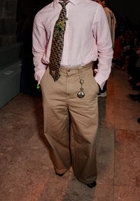 Light pink long-sleeved shirt, patterned blue tie, and tan wide-leg trousers with a pocket watch hanging from a chain.