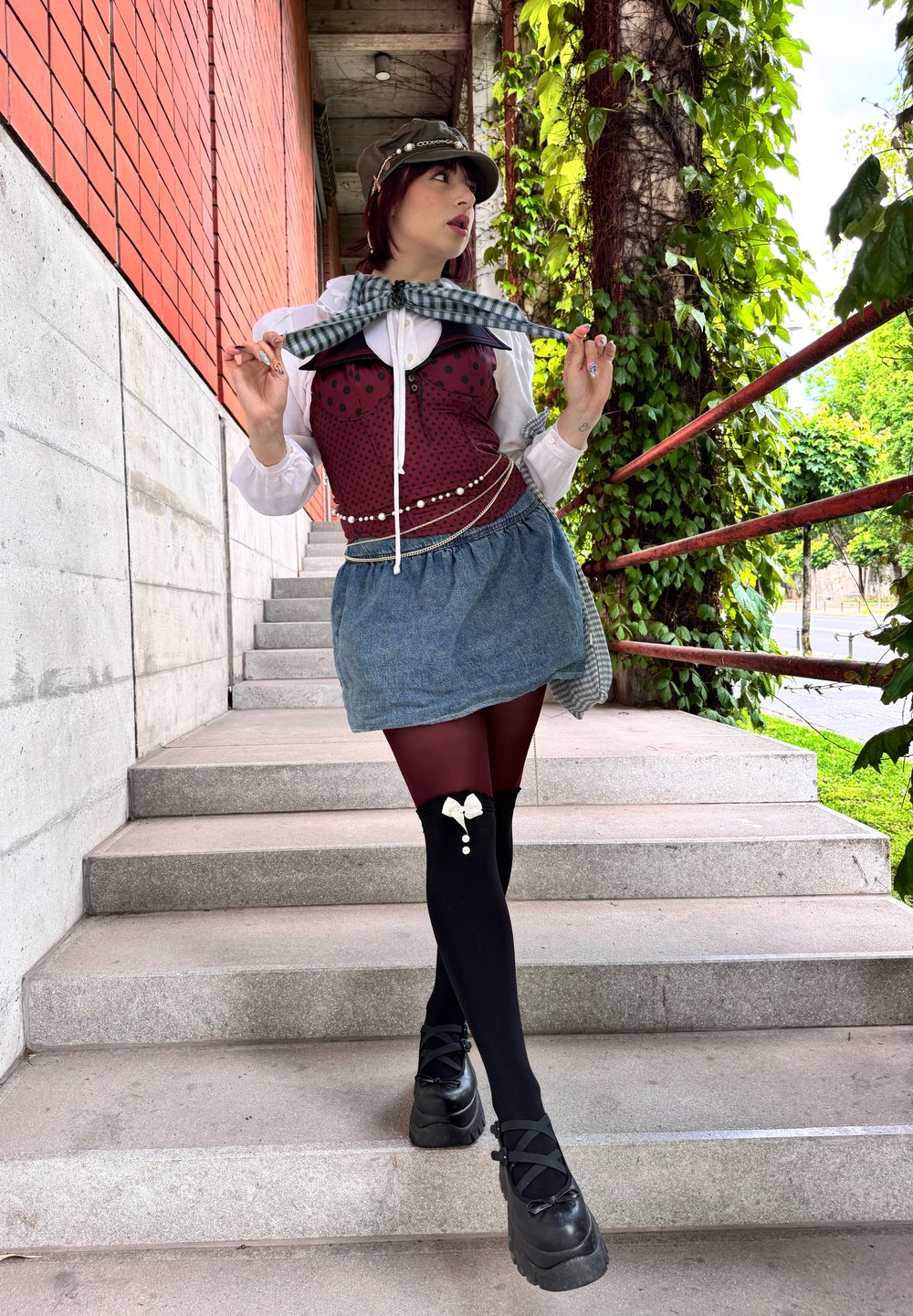 Een kastanjebruine top met zwarte stippen, een denimrok, zwarte panty’s met strikdetail en chunky zwarte schoenen, gecombineerd met een geruite sjaal.