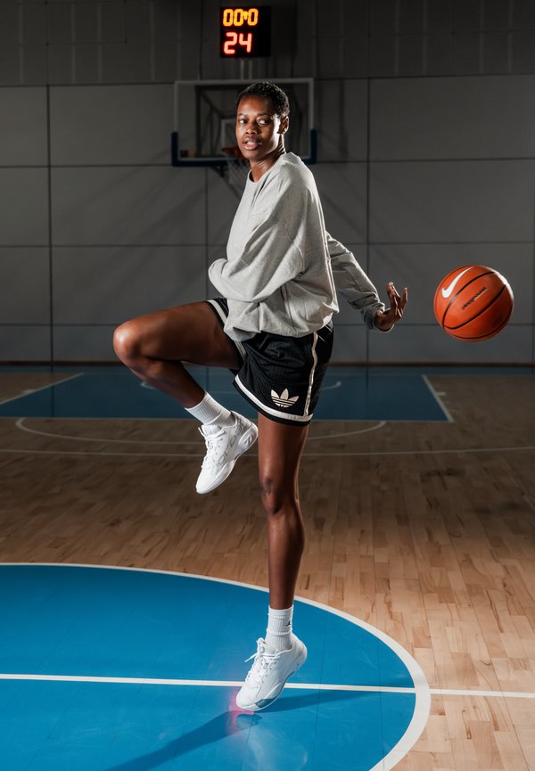 Γυναίκα παίκτρια μπάσκετ με γκρι φούτερ και μαύρο σορτς, που οδηγεί την μπάλα στη μέση του γηπέδου, με το πίνακα αποτελεσμάτων να δείχνει 0:00 και 24 δευτερόλεπτα.