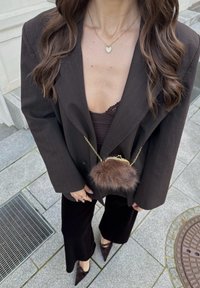 Zwarte oversized blazer met krijtstrepen over een bruin kanten topje, gecombineerd met zwarte uitlopende broek en puntige hakken. Opvallende tas met bontaccent en gesp.