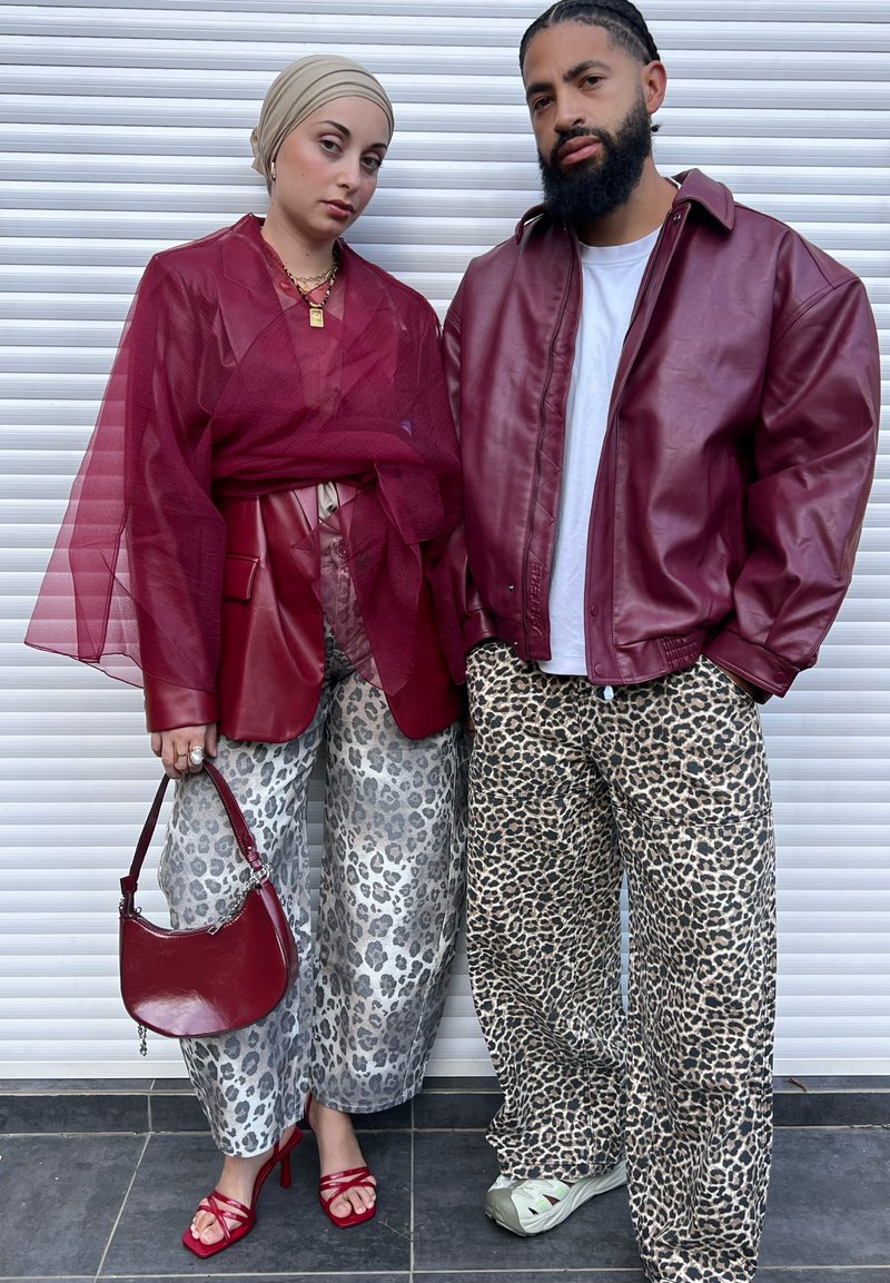 Red leather jacket over a white shirt; maroon sheer top; gray leopard-print pants; red sandals; burgundy bag; background with white blinds.