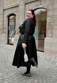 Μαύρη, πλισέ μίντι φούστα συνδυασμένη με μια λαμπερή μαύρη μπλούζα. Αξεσουάρ περιλαμβάνουν μια λευκή τσάντα με χάντρες και μοτίβο σε ανατομικά παπούτσια.