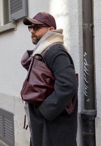 Tummanharmaa villakangastakki, jonka alla kerma- ja harmaakuvioinen huivi, kädessä viininpunainen kudottu nahkalaukku, päässä sopiva lakki ja aurinkolasit.