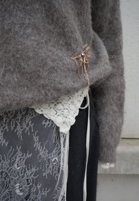 Pull gris duveteux avec une jupe superposée en dentelle blanche, ornée de plusieurs broches fines en chaînes dorées suspendues à l'ourlet du pull.