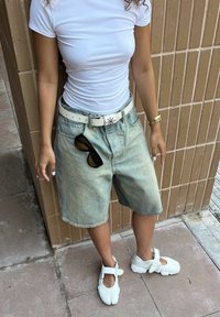 Calções de denim azul-claro com uma textura desbotada, combinados com uma t-shirt branca justa e sapatos brancos. Um cinto branco com fivela e óculos de sol pretos.