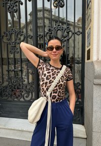 Haut ajusté en imprimé léopard avec des finitions noires, assorti à un pantalon navy ample. Un sac à épaule beige avec une bandoulière tressée complète la tenue.