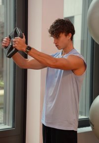 Black weight plate held in the hands of a person wearing a light blue sleeveless top and black shorts, focused on an exercise.