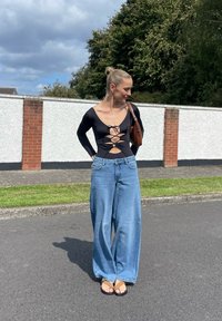 Czarny bodysuit z długim rękawem z wiązaniem z przodu, w połączeniu z jasnoniebieskimi spodniami o szerokich nogawkach i czarnymi sandałami. Brązowa torebka na ramieniu.