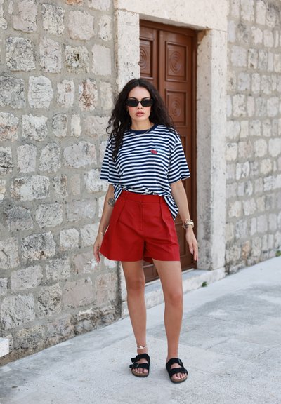Camiseta de rayas azul marino y blanca de gran tamaño con un pequeño corazón rojo, combinada con pantalones cortos rojos de cintura alta y sandalias negras con un acento de lazo.