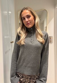 Pull gris ajusté avec un col haut et une patte de boutonnage, en matériau texturé. Porté avec un pantalon imprimé léopard.