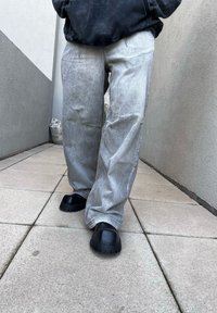 Ανοιχτό γκρίζες φαρδιές τζιν με ορατές ραφές, συνδυασμένες με μαύρες χοντρές παντόφλες με παχύ, αυλακωτό πάτο.