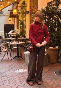 Veste en velours côtelé rouge avec un col montant, associée à un pantalon large marron à fines rayures et des sabots en bois. Comprend des gants gris et un petit sac.