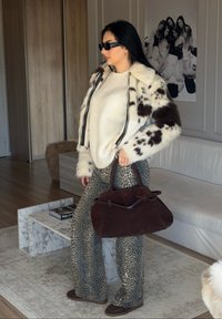 Giacca in pelliccia sintetica bianca e marrone con zip, maglione crema, pantaloni con motivo e borsa marrone scuro. Superfici texture e colori a contrasto.