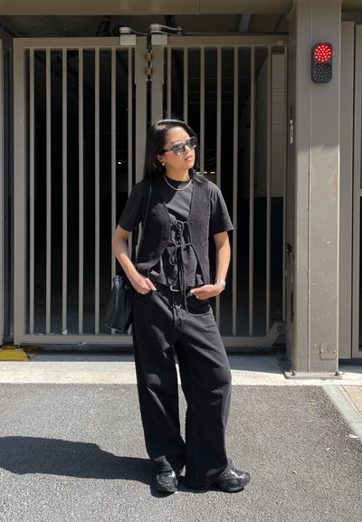 Pantalones oversized negros combinados con una camiseta negra de manga corta y un chaleco negro texturizado. Zapatillas negras y gafas de sol completan el look.