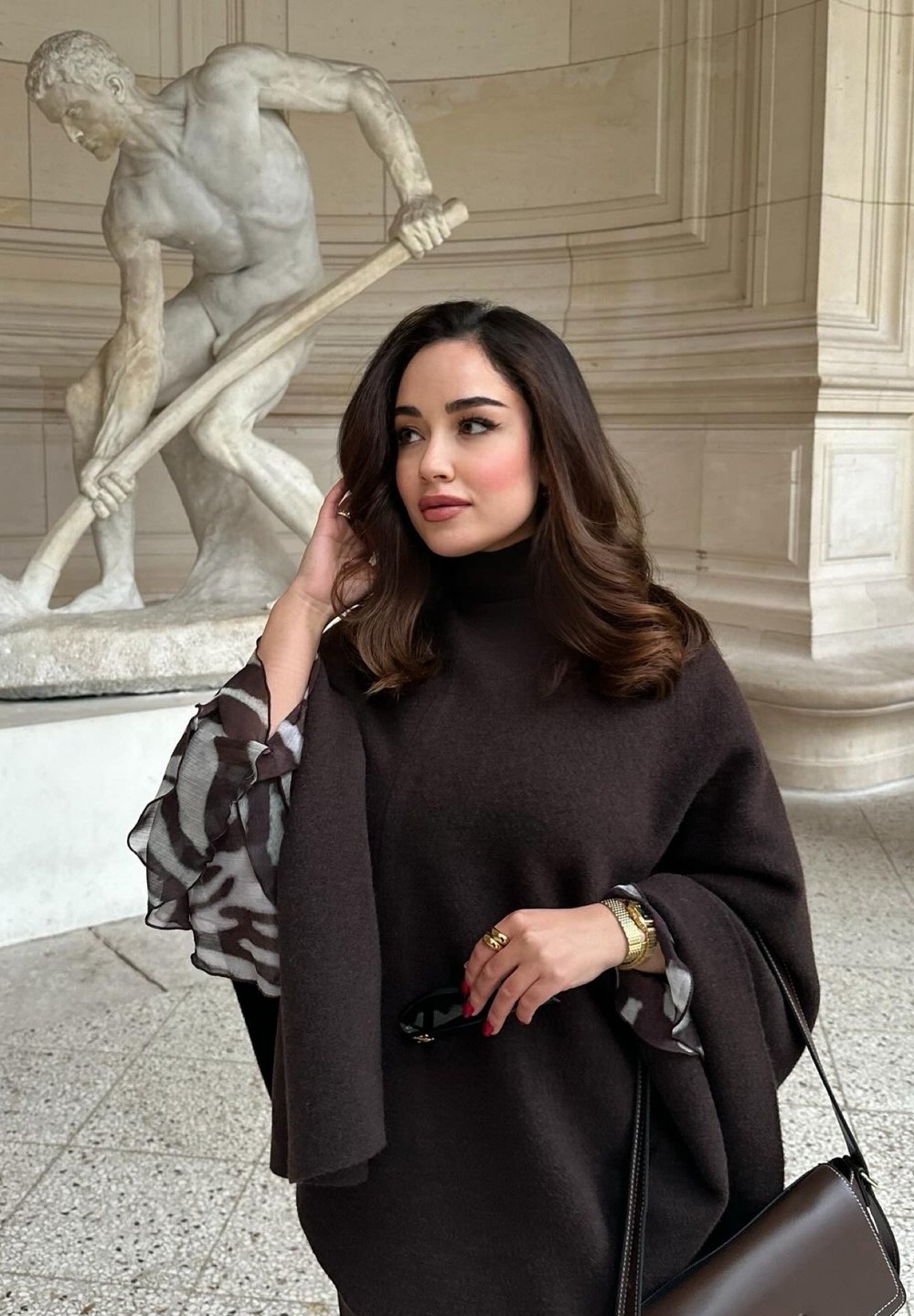 Καφέ μάλλινο πόντσο με φουσκωτά μανίκια και επένδυση από patterned chiffon. Συνοδεύεται από μια καφέ τσάντα και ένα χρυσό ρολόι.