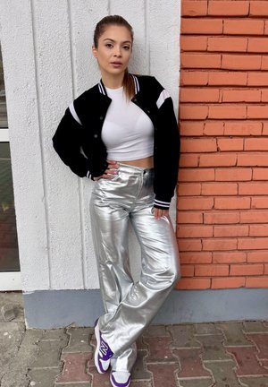 Chaqueta varsity negra con acentos blancos, top corto blanco, pantalones plateados de pierna ancha y brillantes, y zapatillas blancas con detalles morados.