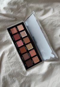 Palette de fards à paupières contenant 12 teintes aux finitions variées, y compris mates et pailletées. Les couleurs vont des roses doux aux bruns riches et aux paillettes.