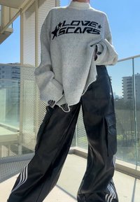 Suéter de punto gris con el texto "LOVE SCARS" en negro. Pantalones de imitación cuero negro con bolsillos cargo y rayas blancas a lo largo de los lados.