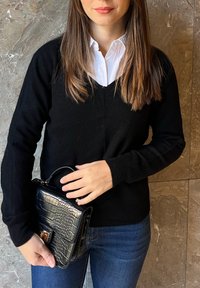 Schwarzer V-Ausschnitt-Pullover über einem weißen Hemd mit Kragen, kombiniert mit einer kleinen schwarzen Handtasche mit Krokodilmuster und goldenen Hardware-Akzenten.