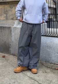 Grå, lette, vandtætte bukser med en løs pasform, hvide piping langs siderne, parret med beige arbejdstøvler og en grå sweatshirt.