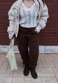 Veste en velours côtelé beige portée sur un haut blanc en maille avec un col en V et des détails en dentelle, associée à un pantalon marron et des bottes noires. Sac vert clair inclus.