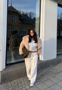 Przytulna szara bluza z zamkiem na suwak na białym krótkim topie, zestawiona z luźnymi białymi spodniami i beżowym płaszczem ze sztucznego futra. Przerzucony jest brązowy dziergany dodatek.