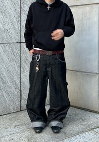 Svart huvtröja tillsammans med lösa, mörka denimjeans. Jeansen har vikta fållar och ett röd-mönstrat b älte med nyckelringsdetaljer.