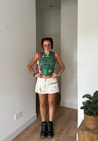 Πράσινο αμάνικο μπλουζάκι με τη λέξη "ΙΤΑΛΙΑ" και τον αριθμό 23, συνδυασμένο με λευκή μίνι φούστα με τσέπες και μαύρες χοντρές μπότες.