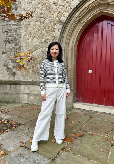 Cárdigan a rayas en blanco y negro con botones redondos, combinado con pantalones blancos de pierna ancha y zapatillas blancas, sobre un fondo de piedra.
