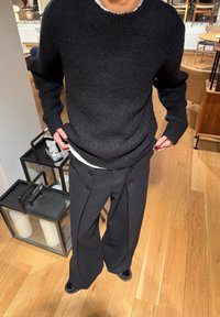 Maglione nero lavorato a maglia con scollo rotondo e vestibilità ampia, abbinato a pantaloni neri a gamba larga con doppio bottone e pieghe frontali.
