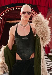 Μαύρο βελούδινο κορμάκι με στρογγυλή λαιμόκοψη και λεπτομέρεια από ρουμπίνια, επενδεδυμένο με πράσινο παλτό με γούνα στην αφή, αξεσουαρισμένο με εντυπωσιακά κοσμήματα.