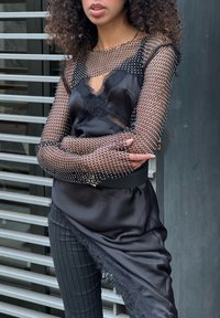 Sort satin top med gennemsigtige netdetaljer, pyntet med perler. Kombiner med stripede bukser og et bredt sort bælte. Har blonder.