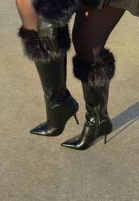 Bottes noires en cuir montant jusqu'aux genoux, avec bouts pointus, talons aiguilles et bordure en fourrure noire douce en haut. Finition brillante, design ajusté.