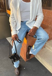 Valge linane nööpidega särk valge topi kohal, hele sinised teksad kulunud mustriga ja pruunid nahast kingad. Must rihmkott üle õla.